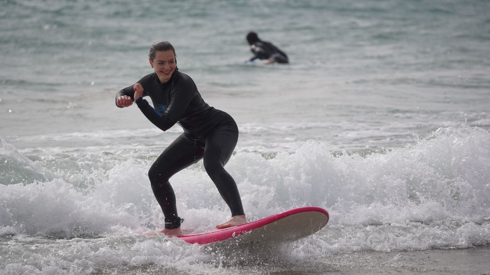 Beginner standing up on a pink soft-top in the whitewater