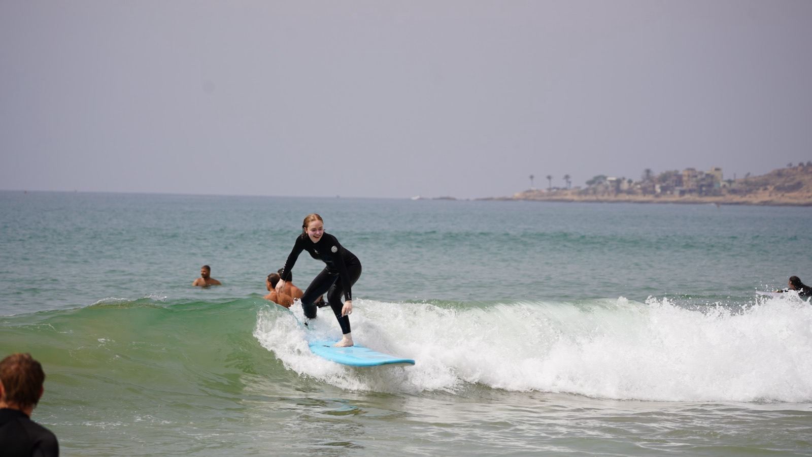 Student riding a green wave on a blue soft-top