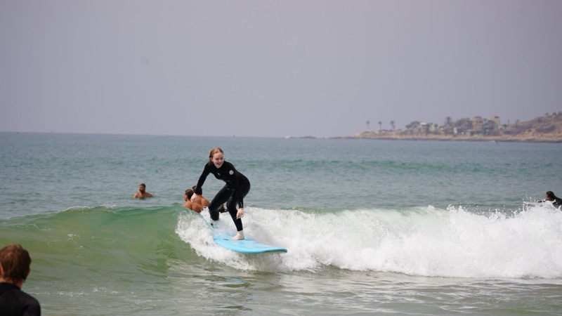 Student riding a green wave on a blue soft-top