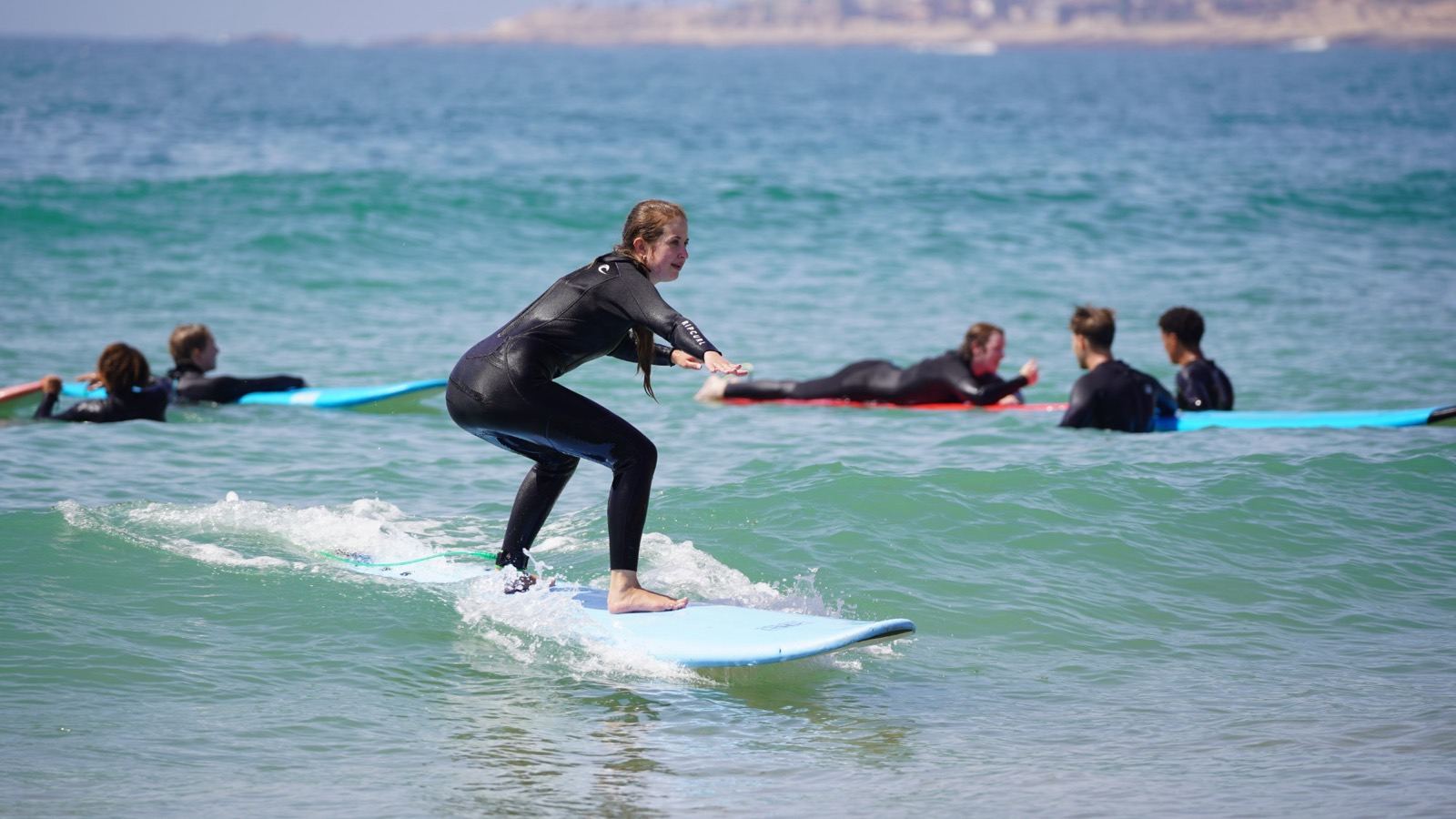 Surf student riding a small wave during a lesson in Taghazout, with the group waiting behind her