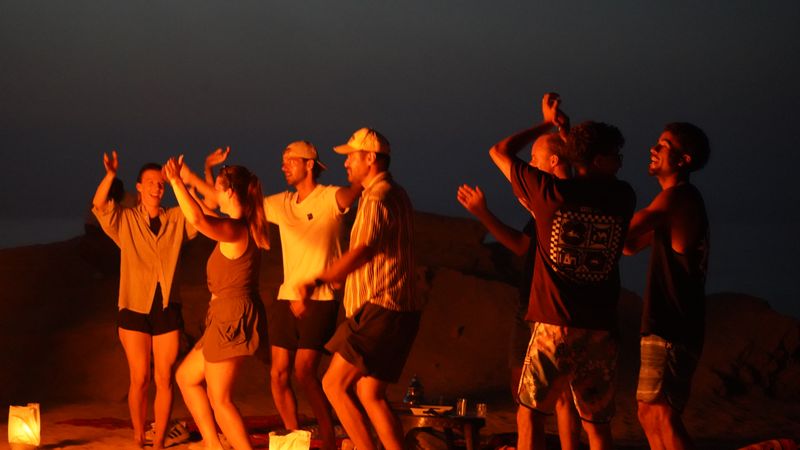 Group dancing and laughing around a bonfire on the dunes at night