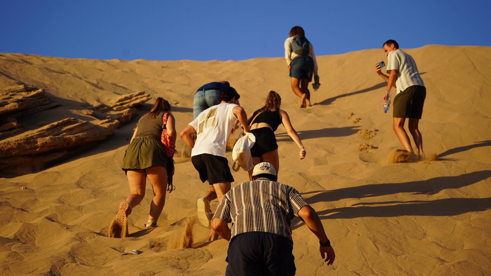Group climbing the big golden dune at Timlaline near Taghazout under a blue sky