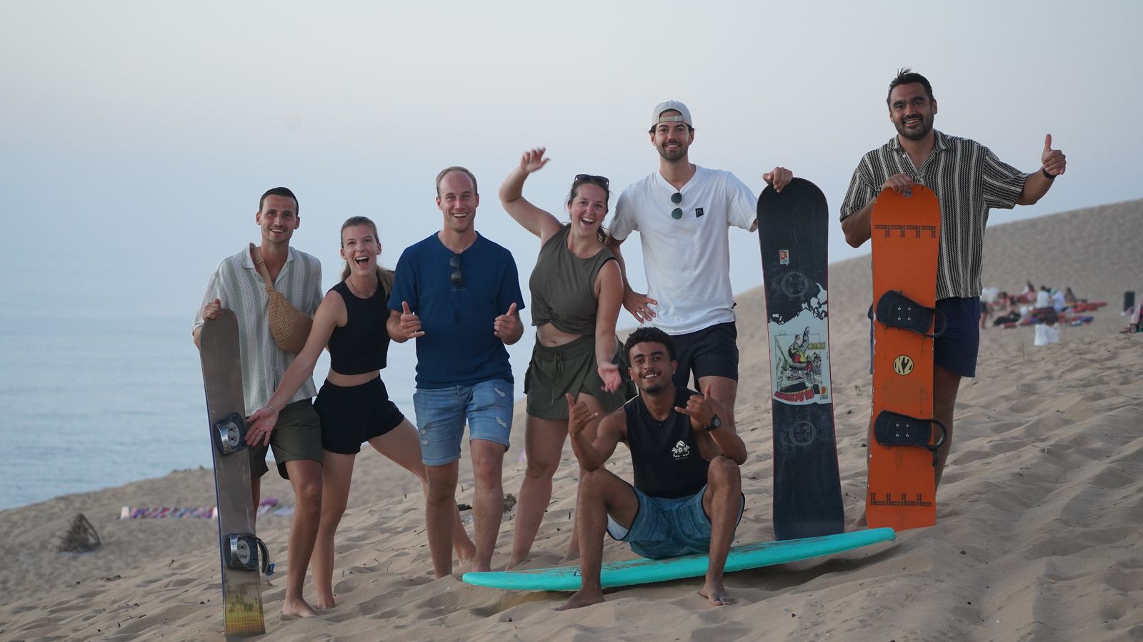 Sandboarding group with their boards on top of the Timlaline dunes near Agadir, the Atlantic Ocean behind them
