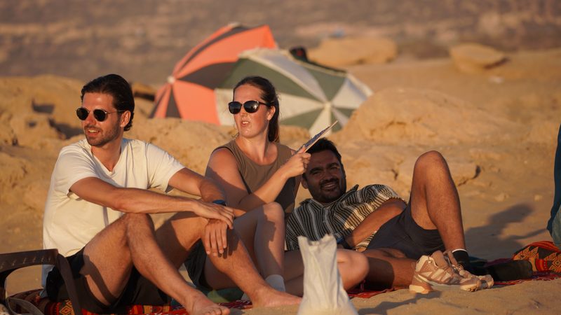 Three guests relaxing on rugs on the dunes in the warm sunset light after sandboarding