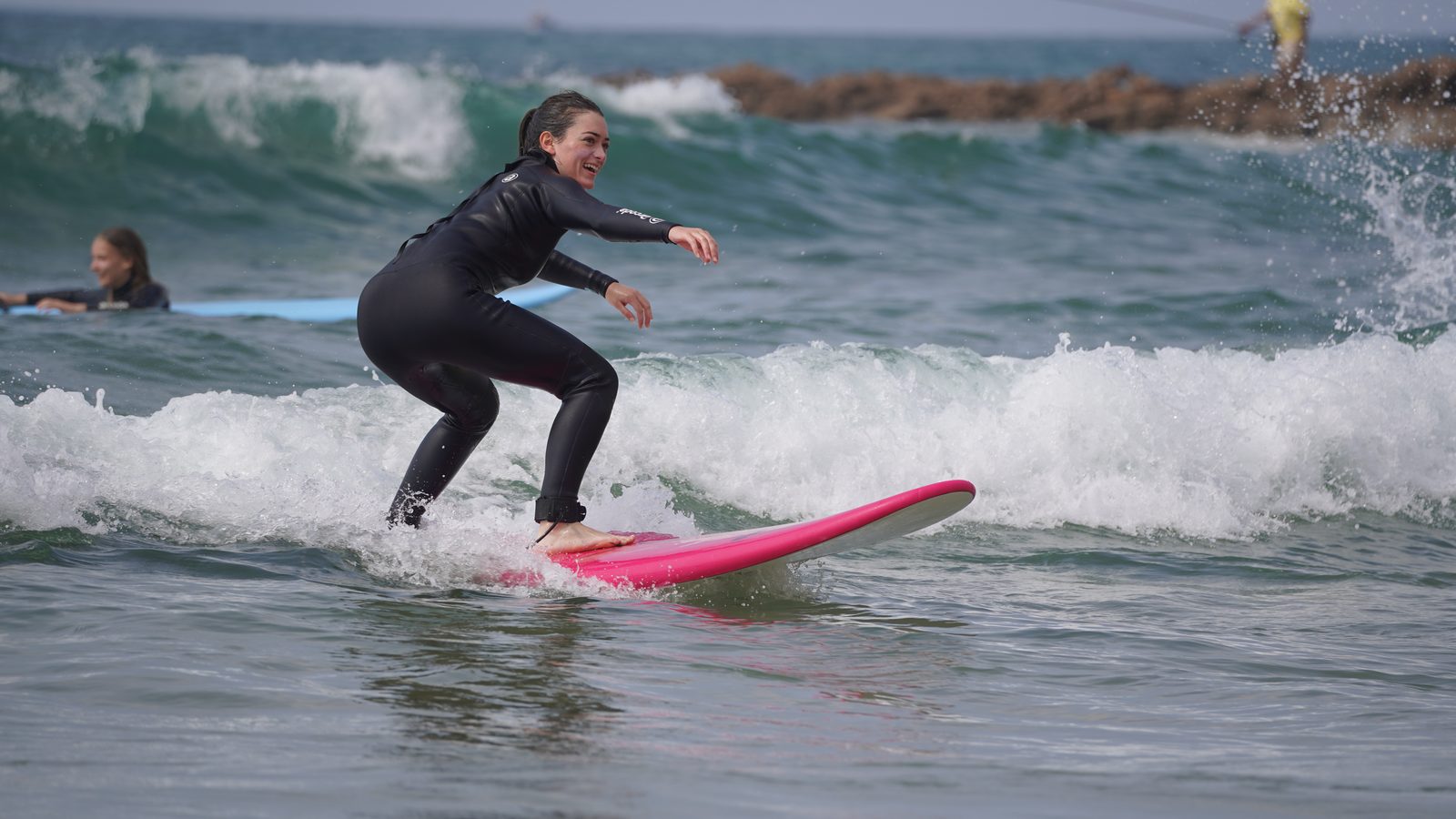Smiling surf student riding a whitewater wave on a pink soft-top board during a beginner lesson near Taghazout