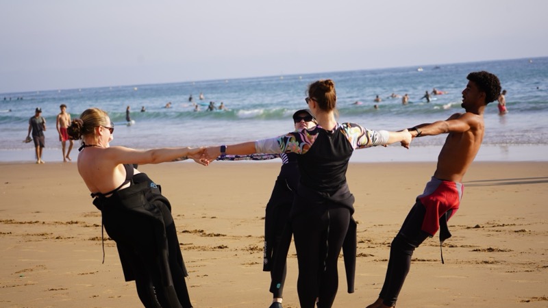 Surf students holding hands in a warm-up circle on the beach before their lesson