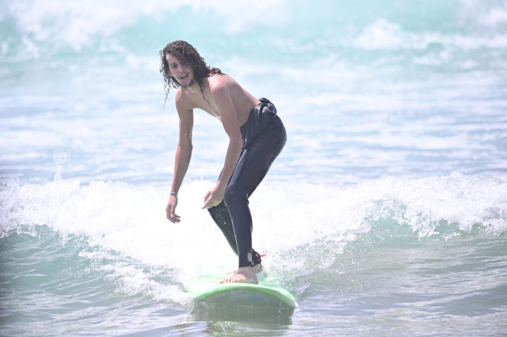 Beginner surfer standing on the board during a surf lesson in Taghazout, Morocco, guided by a professional local surf instructor. Best Surf lessons in Taghazout 